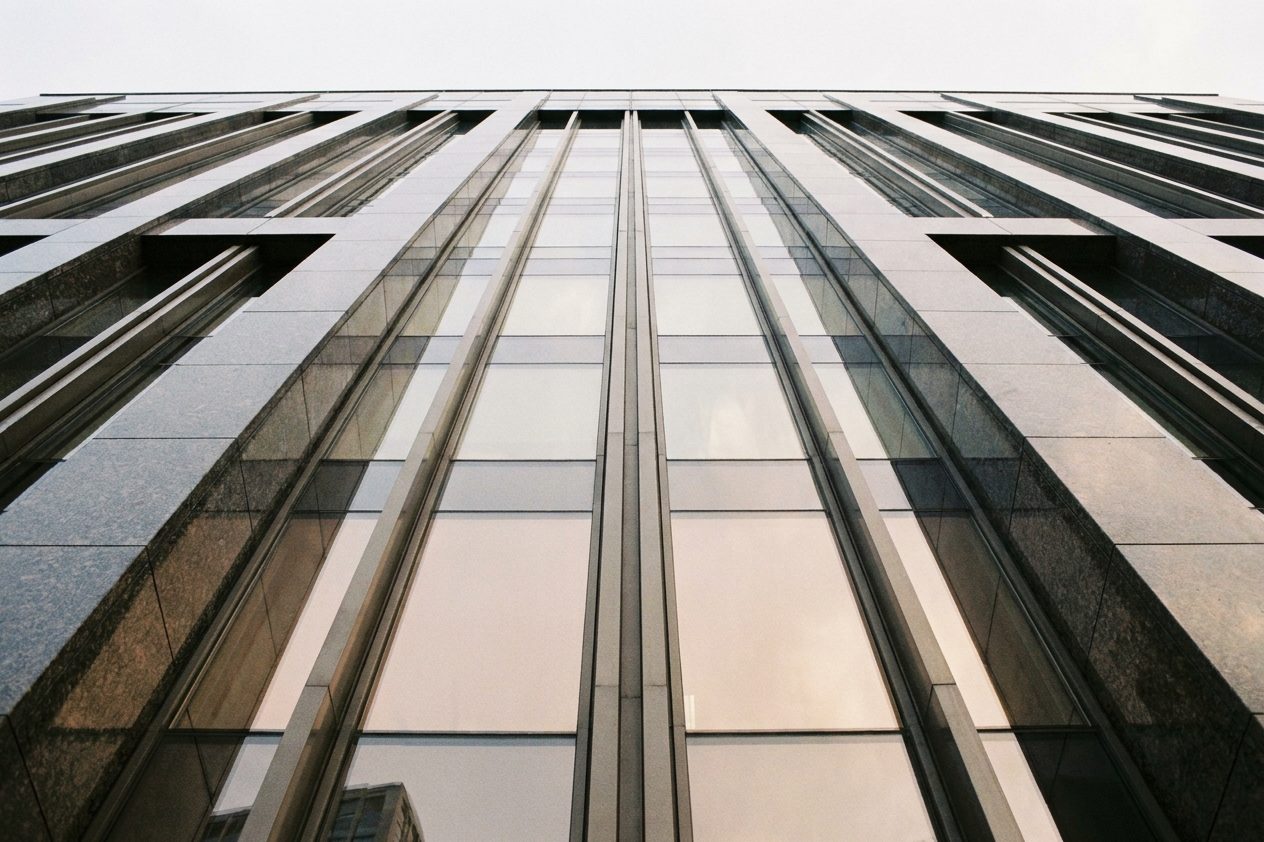 Blick von unten an einer Hochhausfassade aus Granit und Glas entlang nach oben, Himmel darüber.