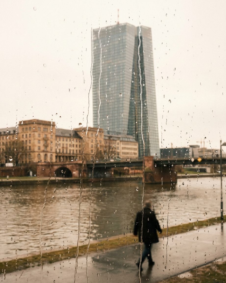 Der EZB-Doppelturm hinter einer regennassen Fensterscheibe, die Tropfen im Vordergrund scharf, das Hochhaus dahinter verschwommen.