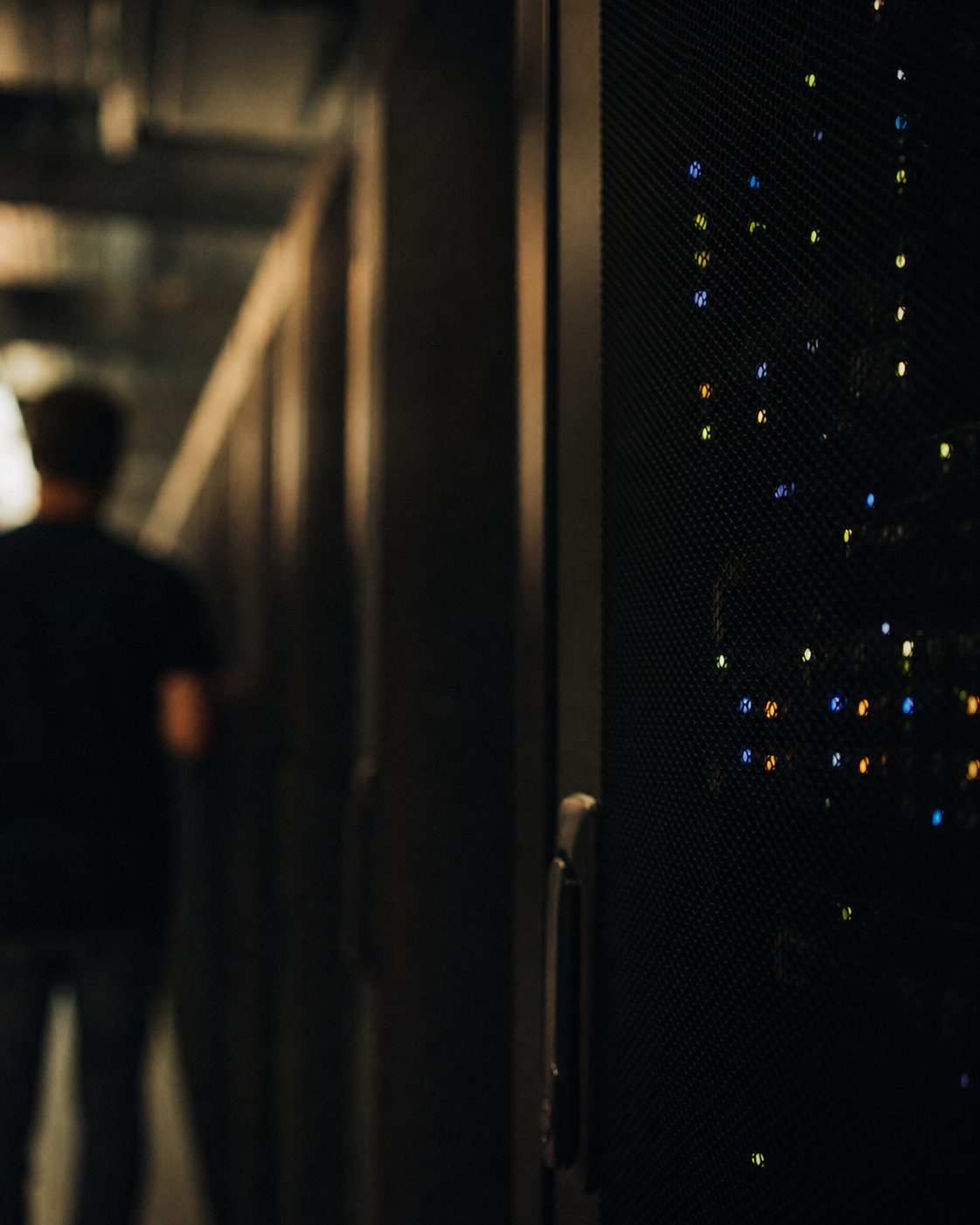 Farbige LED-Lichter eines Serverschranks als unscharfes Bokeh in einem dunklen Rechenzentrum, Hochformat.