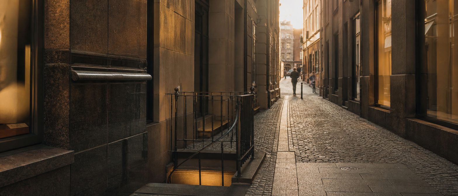 Die schmale Kleine Bockenheimer Straße bei Abendlicht mit einem unscheinbaren Kellerabgang zwischen Geschäftsfassaden.